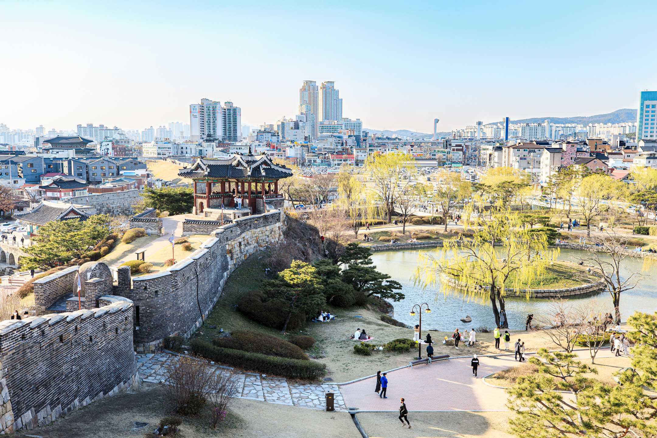 An angle tower that sits on a fortress wall, overlooks a busy pond and stands before a cityscape.